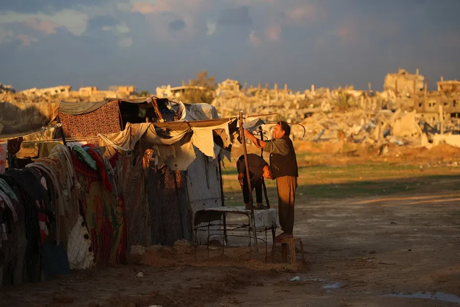 A displaced Palestinian who lost his home in the Gaza war, repairs the covers of his shelter following heavy rains in the Nuseirat refugee camp in the central Gaza Strip on 13 December 2025. (Eyad Baba/AFP)
