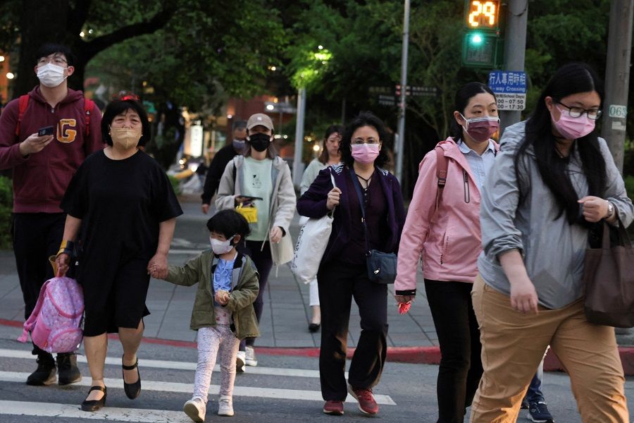 People wearing masks walk across a street in Taipei, Taiwan, 10 April 2023. (I-Hwa Cheng/Reuters)
