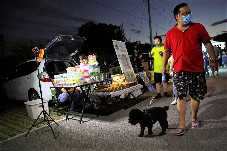 A man walks a dog past a vendor selling fish from a stall at a car boot fair in Beijing, China, 19 August 2022. (Tingshu Wang/Reuters)