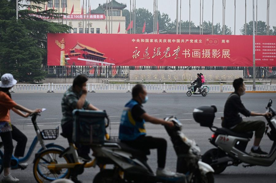In this photo taken on 9 June 2021, people ride past a propaganda slogan which reads "Follow the Party Forever", outside an exhibition of calligraphy, painting and photography celebrating the 100th anniversary of the founding of the Communist Party, at an exhibition centre in Beijing, China. (Greg Baker/AFP)