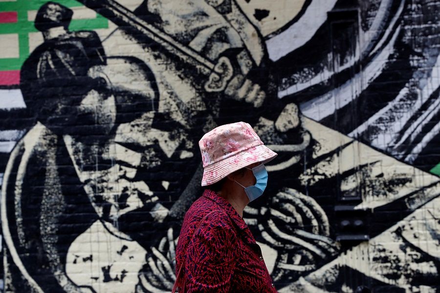 A woman wearing a protective face mask walks by a mural in Manhattan's Chinatown district of New York City, US, 2 June 2021. (Shannon Stapleton/Reuters)