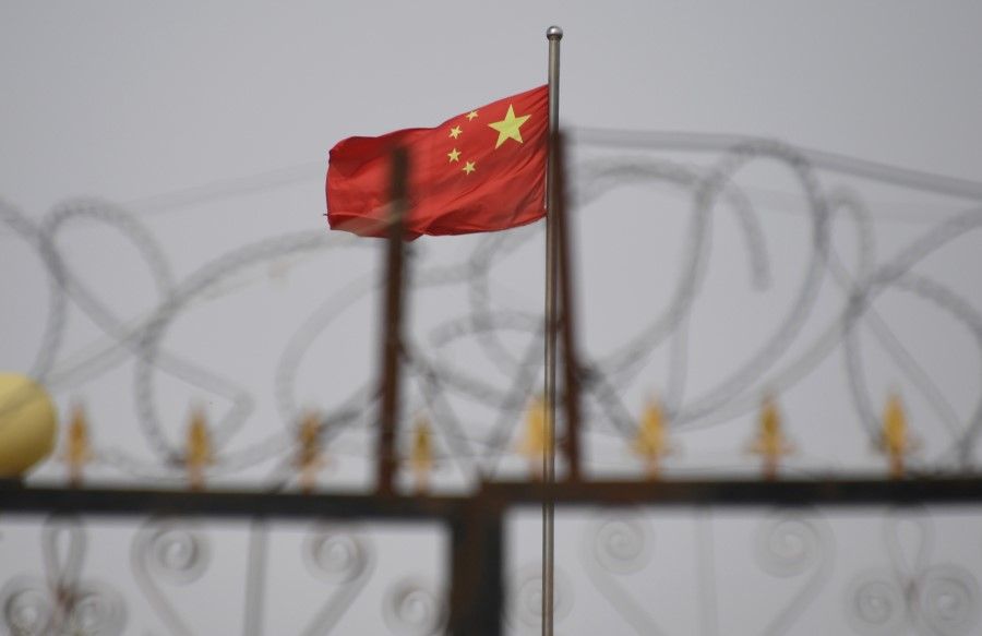 This file photo taken on 4 June 2019 shows the Chinese flag behind razor wire at a housing compound in Yangisar, south of Kashgar, in China's western Xinjiang region. - The US will seize all imports of tomato and cotton products from China's Xinjiang region due to the use of forced labor, the Customs and Border protection agency announced on 13 January 2021. (Greg Baker/AFP)