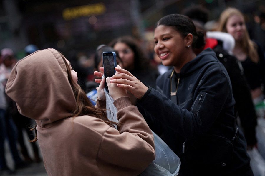 A young woman makes a video of her friends with a mobile phone in Times Square, New York City, US, on 13 March 2024. (Mike Segar/Reuters)