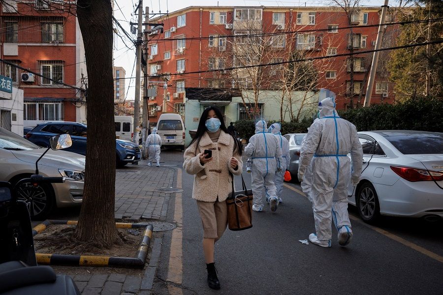 A woman walks past pandemic prevention workers in a neighbourhood where residents do home quarantine, as Covid-19 outbreaks continue in Beijing, China, 8 December 2022. (Thomas Peter/Reuters)