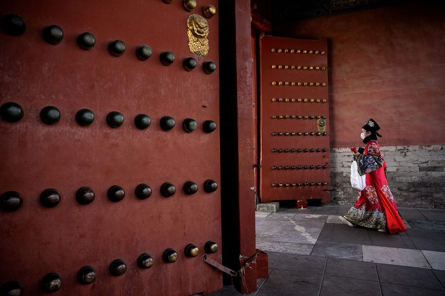 A woman wearing traditional clothes walks past the entrance of the Forbidden City in Beijing, China, on 1 March 2023. (Noel Celis/AFP)