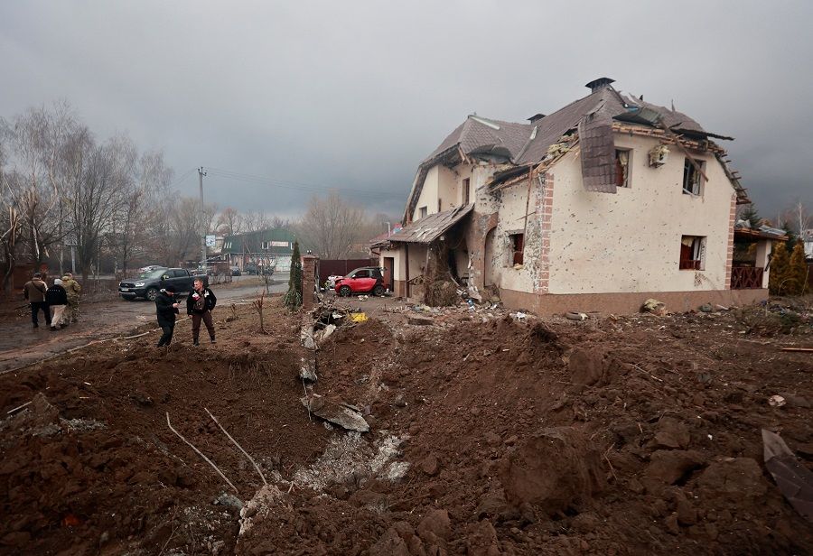 People stand next to a shell crater in front of a house damaged by recent shelling in the village of Hatne, as Russia's invasion of Ukraine continues, in the Kyiv region, Ukraine, 3 March 2022. (Serhii Nuzhnenko/Reuters)