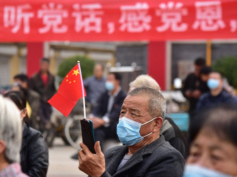 A man holds his phone with a national flag as he watches an outdoor screen showing a live image of the opening session of the 20th Chinese Communist Party Congress in Liaocheng, Shandong province, China, on 16 October 2022. (AFP)