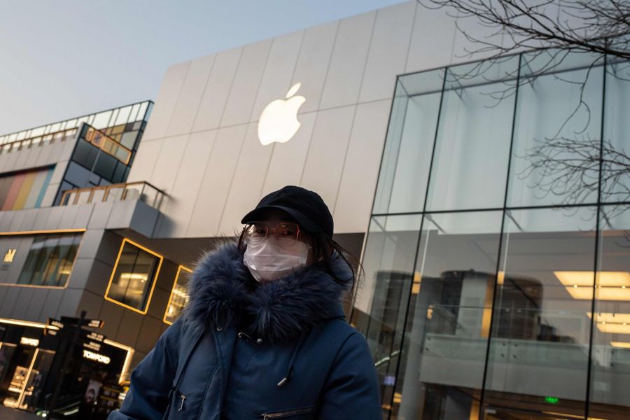 In this file photo taken on 3 February 2020, a woman wearing a protective facemask walks outside of a closed-off Apple Store in Beijing. Apple is expected to to delay the launch of its newest iPhone model originally planned for March this year. (Nicolas Asfouri/AFP)