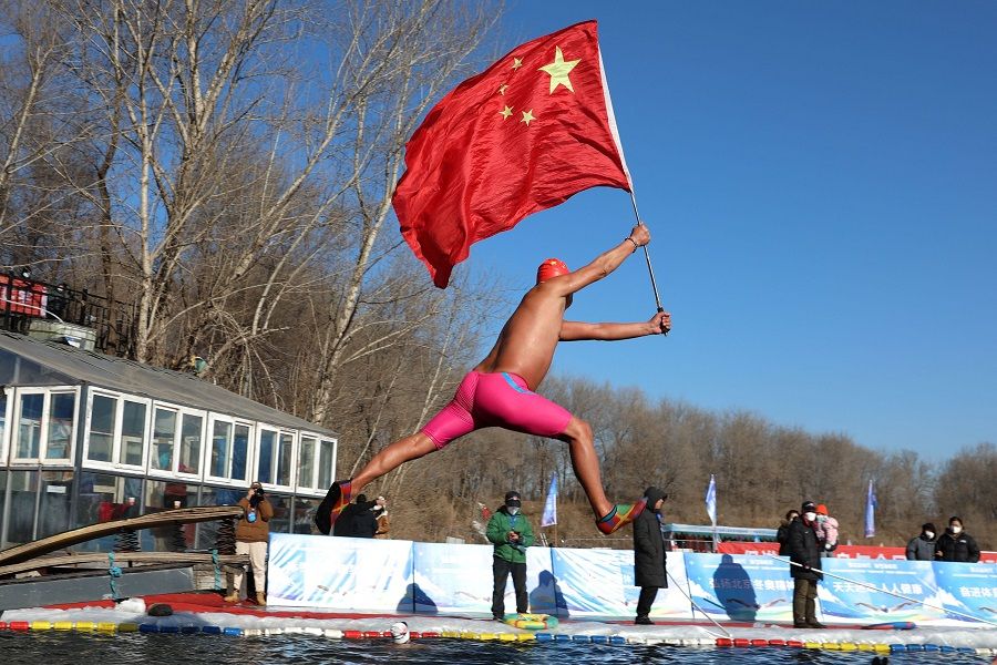 A winter swimming enthusiast holds a Chinese national flag as he dives into a pool cut in the frozen riverbank to celebrate the new year in Shenyang, Liaoning province, China, on 1 January 2023. (AFP)