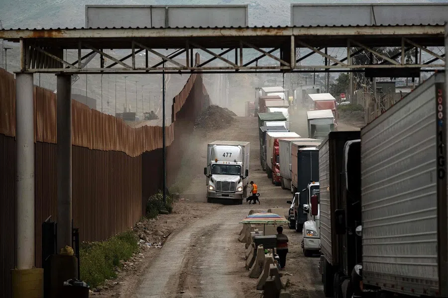 Cargo trucks line up next to the border fence to cross to the US near the US-Mexico border in Tijuana, Baja California state, Mexico, on 4 April 2019. US President-elect Donald Trump said he intends to impose sweeping tariffs on goods from Mexico, Canada and China, prompting a swift warning from Beijing that “no one will win a trade war”. (Guillermo Arias/AFP)