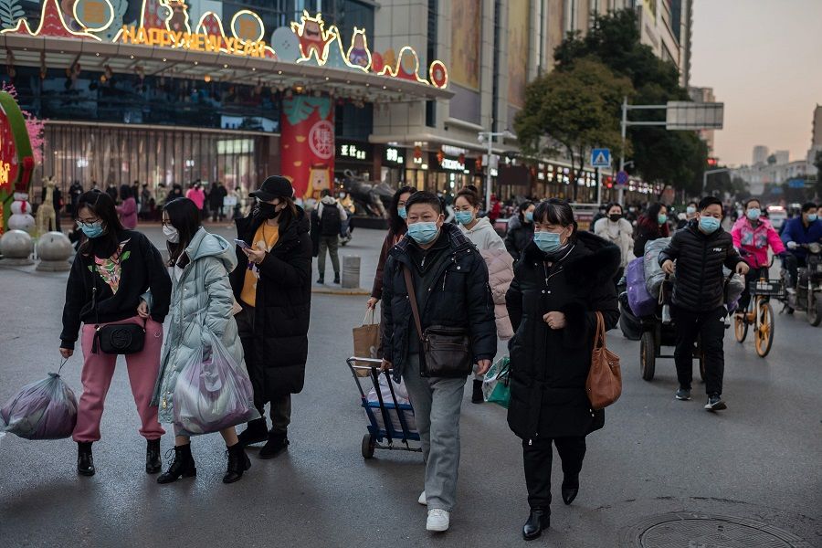 People wearing face masks walk outside of a shopping mall complex during rush hour in Wuhan on 13 January 2021. (Nicolas Asfouri/AFP)