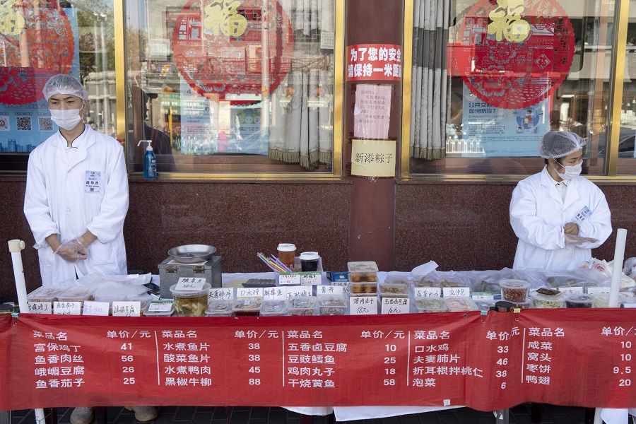 China's F&B industry is badly hit by the Covid-19 pandemic. In this photo taken on 23 April 2020, employees wearing protective masks stand behind takeaway food displayed on a table outside a restaurant in Beijing, China. (Giulia Marchi/Bloomberg)