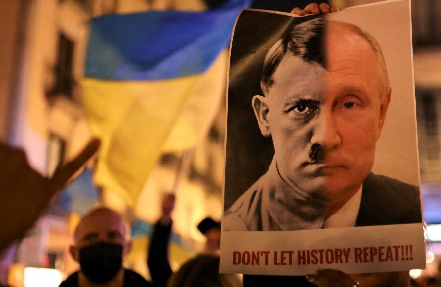 A person holds a banner with the joined faces of a portrait of Vladimir Putin and Nazi dictator Adolf Hitler during an anti-war protest, after Russian President Vladimir Putin authorised a massive military operation against Ukraine, in Barcelona, Spain, 24 February 2022. (Nacho Doce/Reuters)
