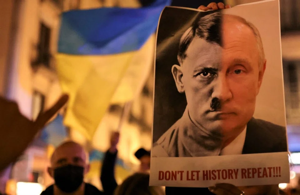 A person holds a banner with the joined faces of a portrait of Vladimir Putin and Nazi dictator Adolf Hitler during an anti-war protest, after Russian President Vladimir Putin authorised a massive military operation against Ukraine, in Barcelona, Spain, 24 February 2022. (Nacho Doce/Reuters)