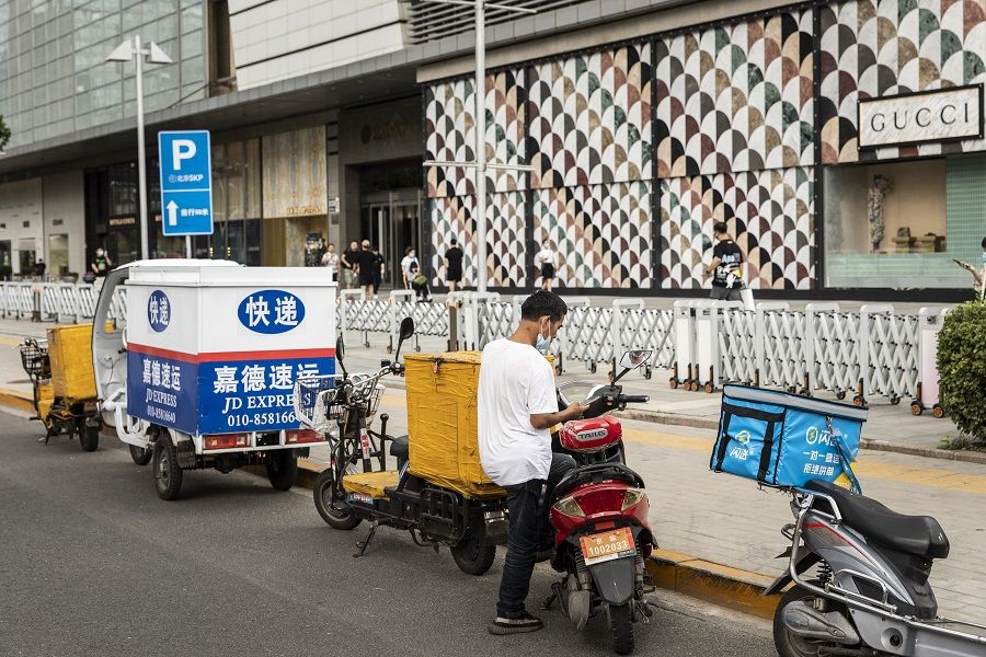 A delivery driver stands with this motorcycle near an upscale shopping mall in Beijing, China on 25 August 2021. (Qilai Shen/Bloomberg)