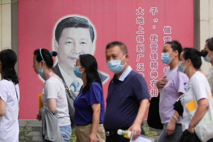 People wearing face masks pass by a portrait of Chinese President Xi Jinping, following the Covid-19 outbreak in Shanghai, China, 31 August 2022. (Aly Song/Reuters)