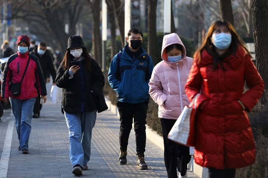 People wearing protective face masks walk on a street during morning rush hour, in Beijing, China, 18 January 2022. (Tingshu Wang/Reuters)