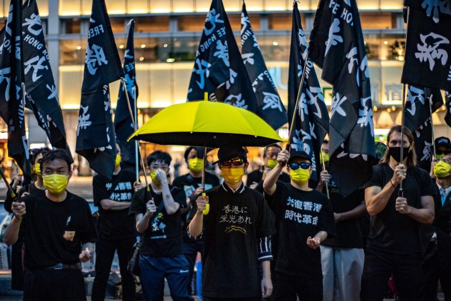 Pro-democracy activists hold a yellow umbrella and flags that read "Free Hong Kong, Revolution Now" outside a train station in Shinjuku district of Tokyo on 4 June 2022, to mark the 33rd anniversary of the 1989 Tiananmen Square crackdown in Beijing. (Philip Fong/AFP)