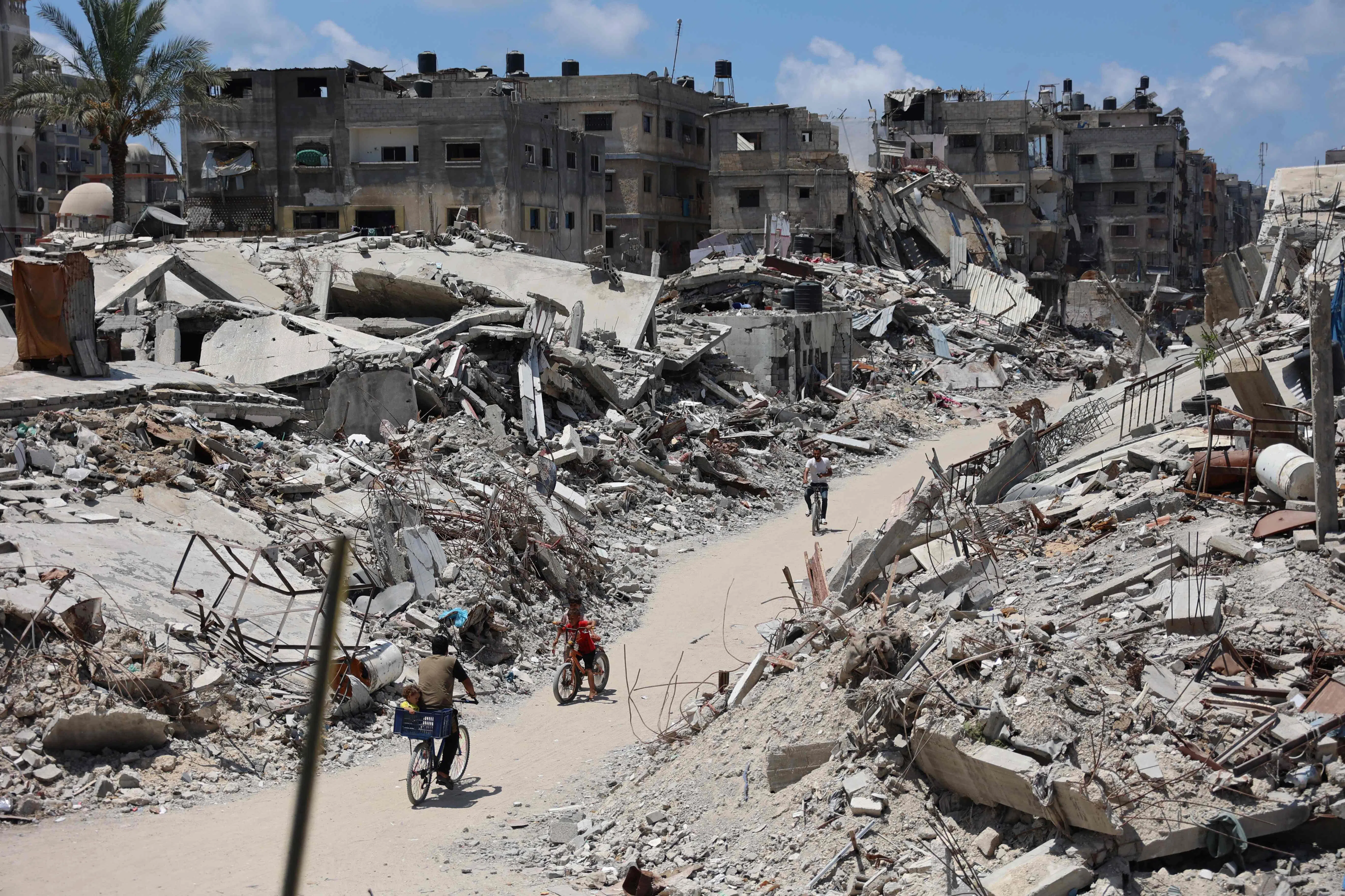 Palestinians cycle past destroyed buildings levelled in previous Israeli military Bombardment of Beit Lahia, in the northern Gaza Strip on 29 July 2024, amid the ongoing conflict between Israel and the Palestinian Hamas militant group. (Omar Al-Qattaa/AFP)