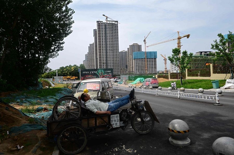 A man rests on a tricycle in front of a housing complex under construction in Xinzheng, Henan province, China, on 20 June 2023. (Pedro Pardo/AFP)