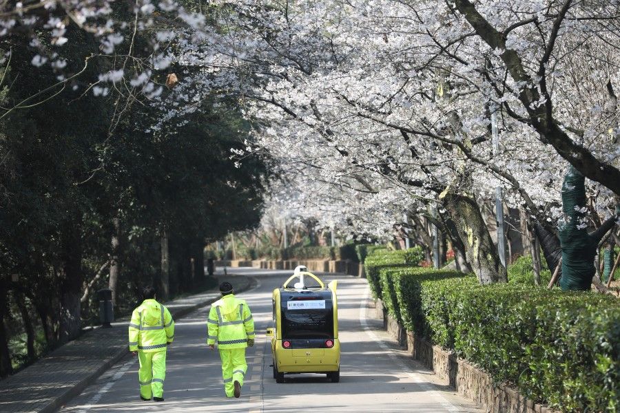 Security personnel walk next to a 5G-enabled autonomous vehicle, installed with a camera filming blooming cherry blossoms for an online livestreaming session, inside the closed Wuhan University, 17 March 2020. (China Daily via REUTERS)