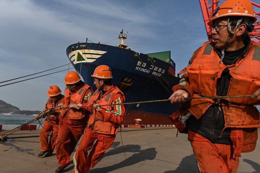 Workers pull a rope as a cargo ship carrying containers docks at the Lianyungang Port Container Terminal in Lianyungang, Jiangsu province, China on 24 March 2021. (Hector Retamal/AFP)