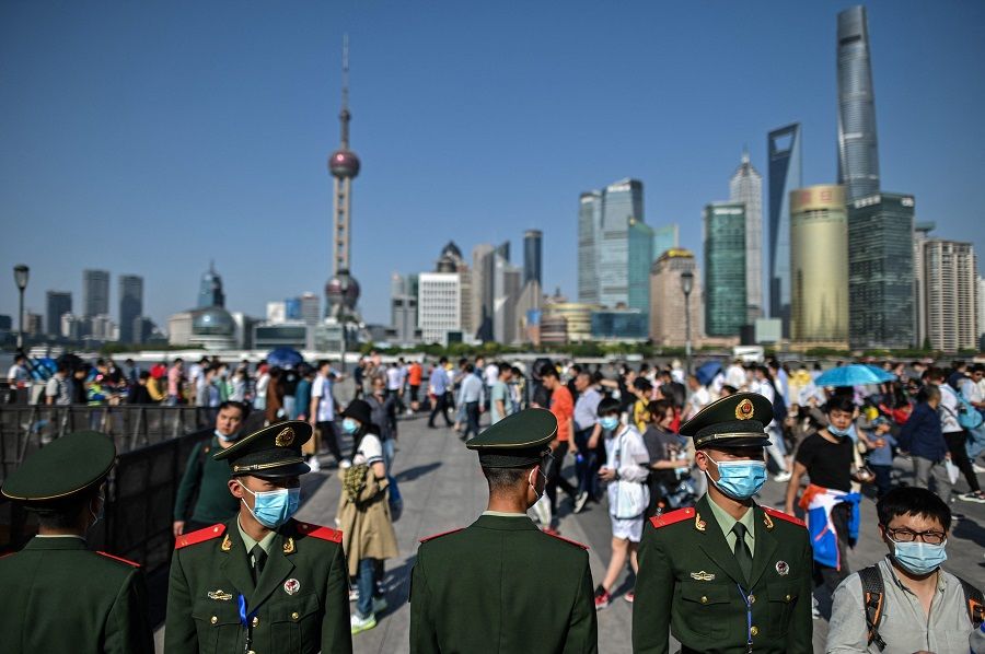 In this picture taken on 1 May 2021, Chinese paramilitary police keep watch as people visit the promenade on the Bund along the Huangpu River during the Labour Day holiday in Shanghai, China. (Hector Retamal/AFP)