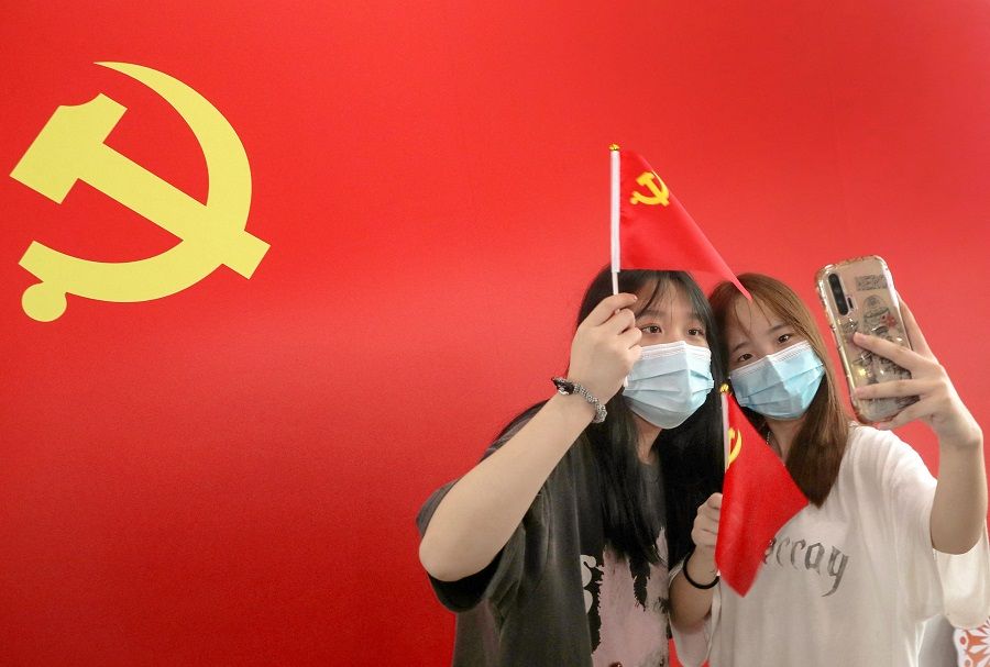 Commuters take photos with a flag of the Communist Party of China at Nantong Railway Station, Jiangsu province, China on 1 July 2021, during celebrations to mark the 100th anniversary of the founding of the Communist Party of China. (STR/AFP)