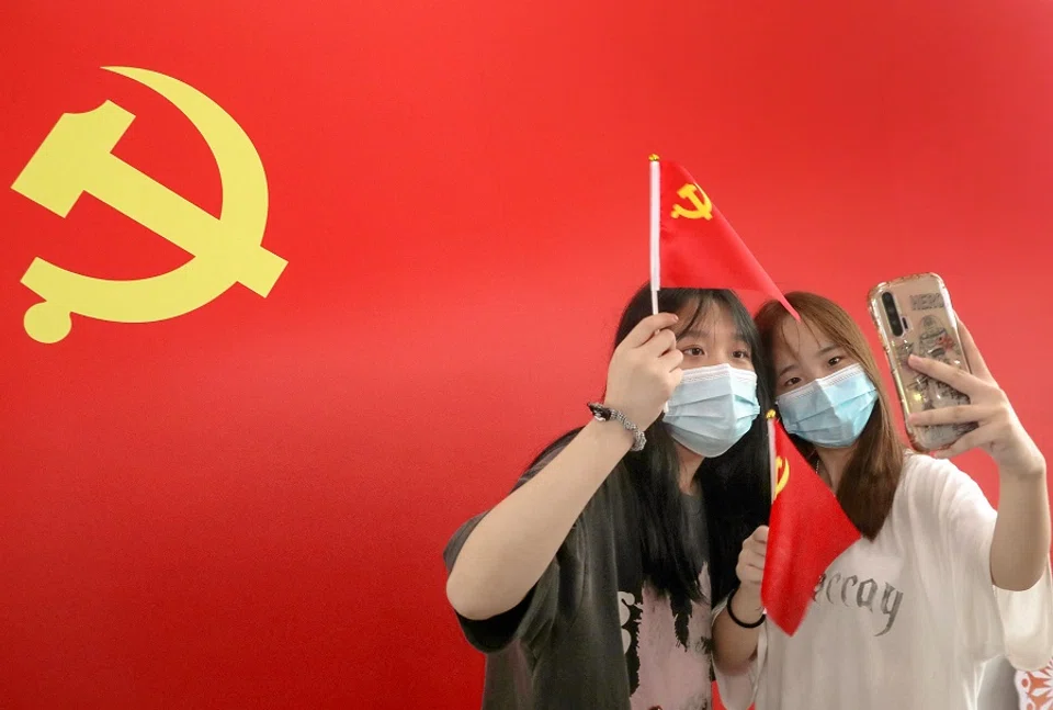 Commuters take photos with a flag of the Communist Party of China at Nantong Railway Station, Jiangsu province, China on 1 July 2021, during celebrations to mark the 100th anniversary of the founding of the Communist Party of China. (STR/AFP)