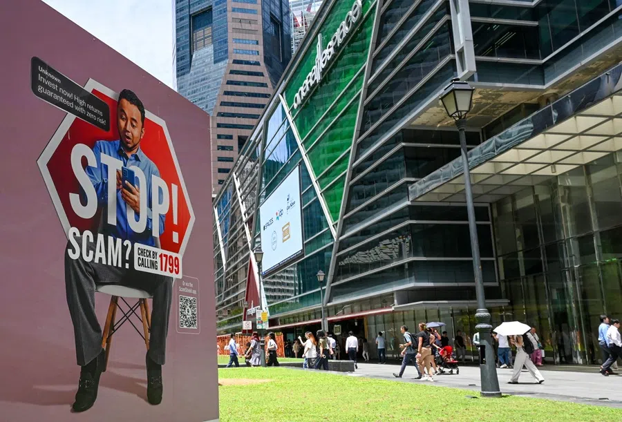 People walk past a poster warning of scam threats in the financial business district of Raffles Place in Singapore on 3 September 2025. (Roslan Rahman/AFP)