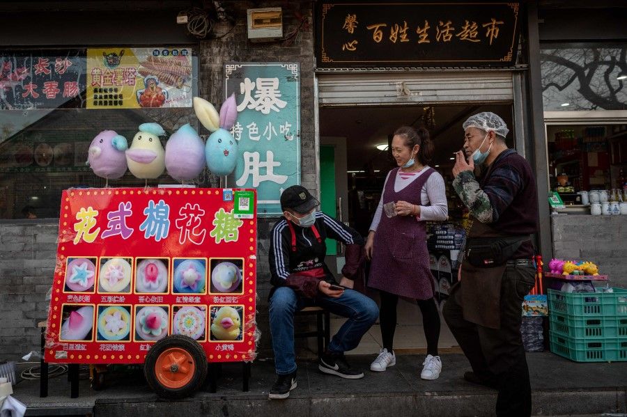 Restaurant workers (right) chat with a cotton candy vendor (left) during their break along a street in a traditional neighbourhood in Beijing on 4 April 2021. (Nicolas Asfouri/AFP)