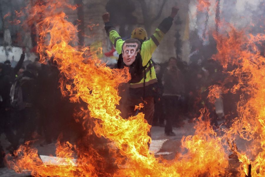 A Yellow Vest protester wearing a mask depicting the French President on which is written 'psycho', gestures behind flames rising from barricades, in Paris on March 16, 2019, during the 18th consecutive Saturday of demonstrations called by the 'Yellow Vest' (gilets jaunes) movement. The movement is a nationwide protest against the French President's policies and his top-down style of governing, high cost of living, government tax reforms, and for more "social and economic justice." (Zakaria Abdelkafi/AFP)