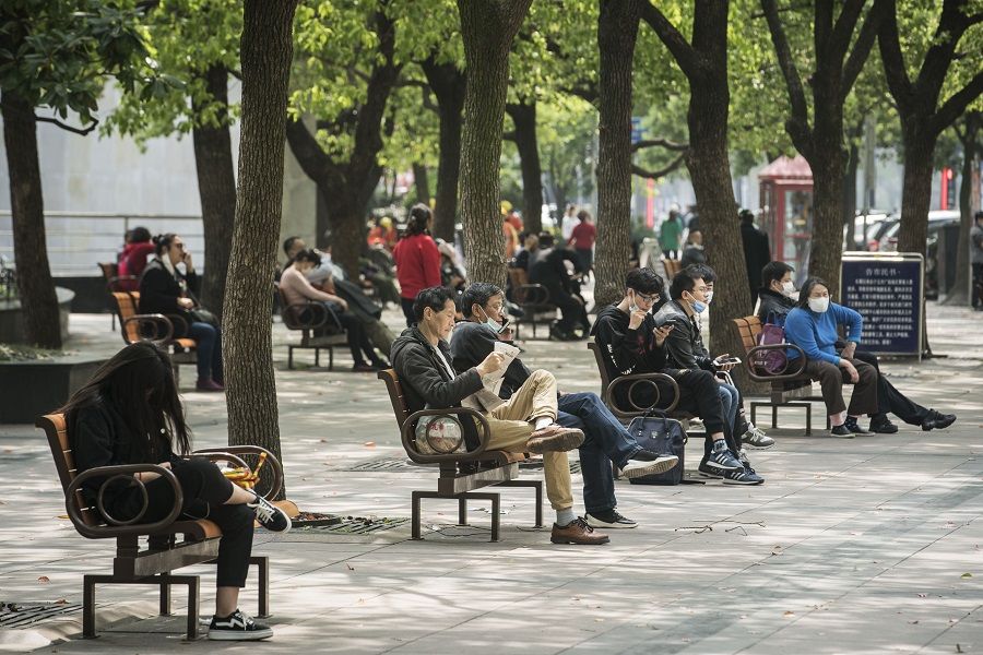 People, some wearing protective masks, sit on benches along Nanjing Road in Shanghai, China, on 20 April 2020. (Qilai Shen/Bloomberg)