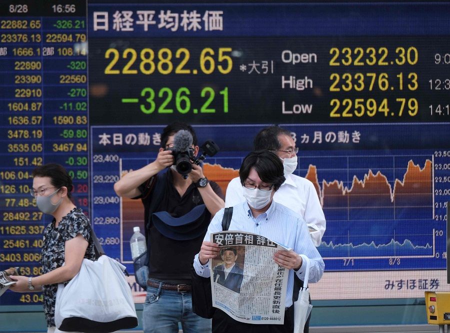 A pedestrin reads an extra edition of Japan Prime Minister Shinzo Abe's resignation in front of an electronic quotation board displaying share prices from the Tokyo Stock Exchange in Tokyo on 28 August 2020. (Kazuhiro Nogi/AFP)