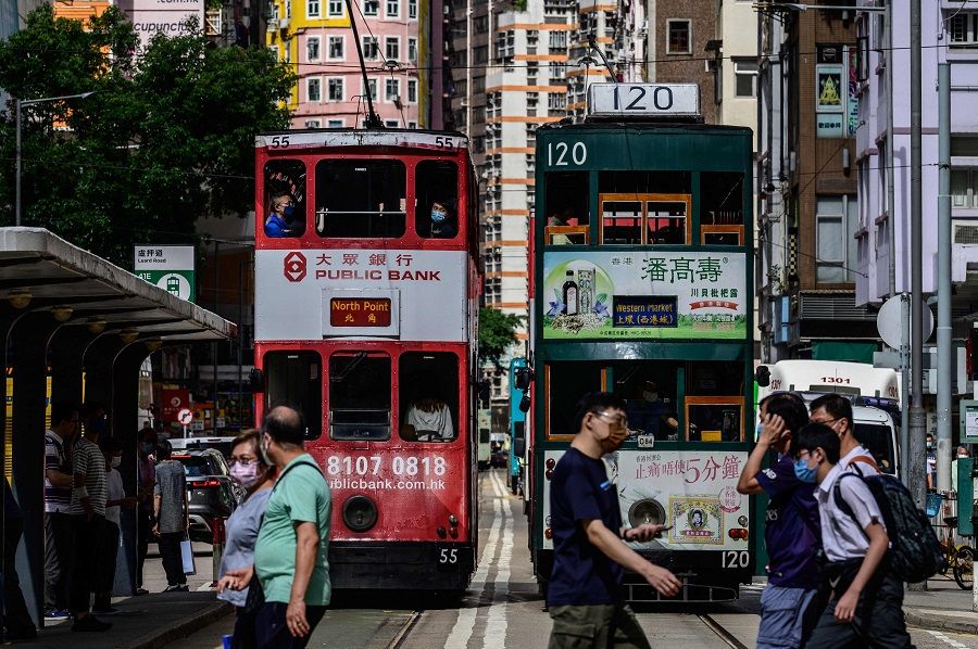 Pedestrians walk across a road in front of commuter trams in Hong Kong on 11 May 2021. (Anthony Wallace/AFP)