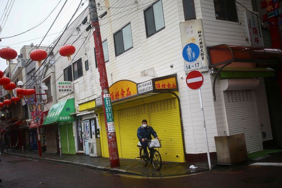 A man wearing protective face mask following an outbreak of the Covid-19 pandemic rides on his bicycle on an almost empty street in Yokohama's Chinatown, Tokyo, Japan on 10 March 2020. (Edgard Garrido/Reuters)