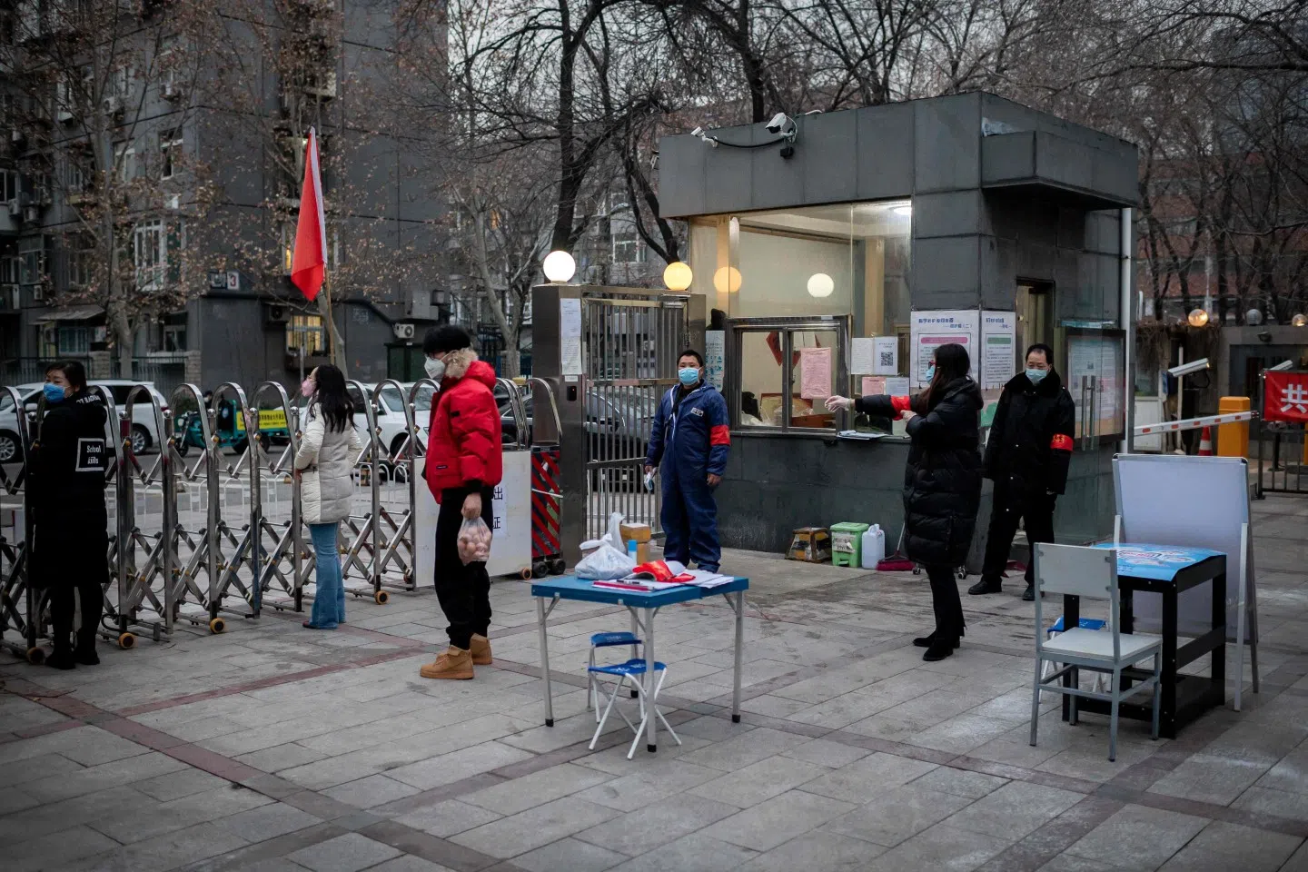 Security officers and residents wearing protective facemasks to protect against the Covid-19 coronavirus stand at the entrance of a residential compound where temperature and special access passes are needed to enter or exit, in Beijing on 24 February 2020.(Nicolas Asfouri/AFP)