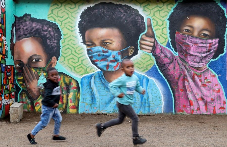 Boys run past a mural by Senzart911, of children wearing facemasks amid the coronavirus disease (Covid-19) outbreak, at Soweto's Kliptown, South Africa, 27 October 2021. (Siphiwe Sibeko/Reuters)