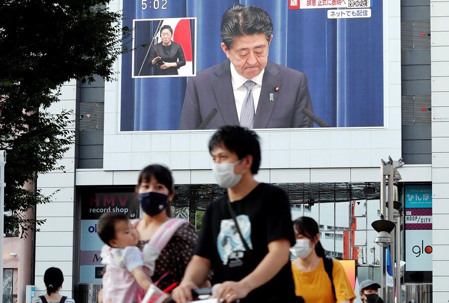 People wearing protective face masks walk past a large screen broadcasting a news conference of Japan Prime Minister Shinzo Abe in Tokyo, Japan, 28 August 2020. (Kim Kyung-Hoon/Reuters)