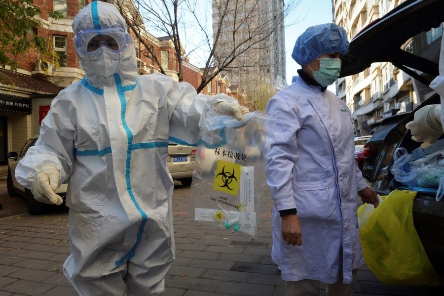 A medical worker in a protective suit holds a plastic bag with swab samples in Tianjin on 22 November 2020, after new coronavirus cases were detected in the city. (STR/AFP)