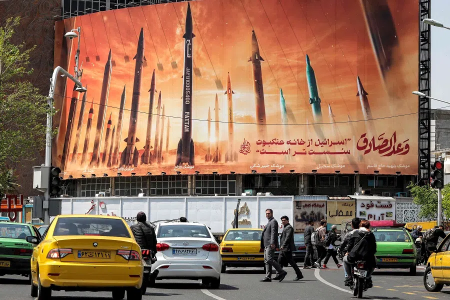 Motorists drive their vehicles past a billboard depicting named Iranian ballistic missiles in service, with text in Arabic reading "the honest [person's] promise" and in Persian "Israel is weaker than a spider's web", in Valiasr Square in central Tehran, Iran, on 15 April 2024. (Atta Kenare/AFP)