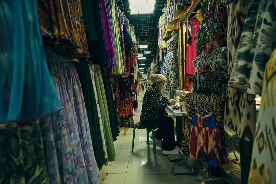 On the third floor of Jinquan Shopping Mall, a Uighur woman works her craft on a sewing machine at the entrance of a store, stitching together brightly colored traditional garments.