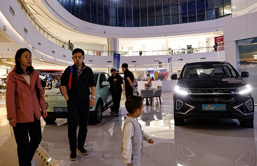 People walk past electric vehicles at a shopping mall in Beijing, China, on 3 November 2023. (Tingshu Wang/Reuters)