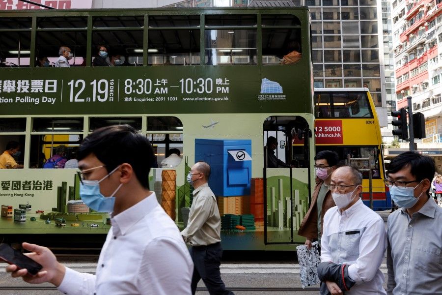 People walk in front of a tram with an advertisement about upcoming Legislative Council election in Hong Kong, China, 16 November 2021. (Tyrone Siu/Reuters)