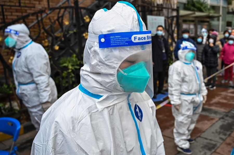 Workers wearing protective gear look on as people wait to be tested for the Covid-19 coronavirus at a residential compound in Shanghai, China, on 18 March 2022. (Hector Retamal/AFP)