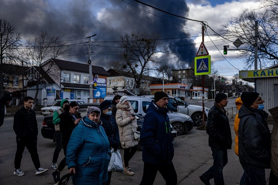 People stand in line in front of a supermarket while smoke billows over the town of Vasylkiv just outside Kyiv, Ukraine, on 27 February 2022, after overnight Russian strikes hit an oil depot. (Dimitar Dilkoff/AFP)
