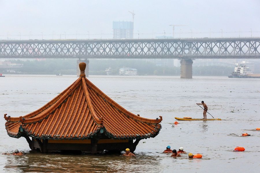 People (foreground) swim in the swollen Yangtze River as the roof of an inundated pavilion is seen above floodwaters in Wuhan, Hubei, on 8 July 2020. (STR/AFP)