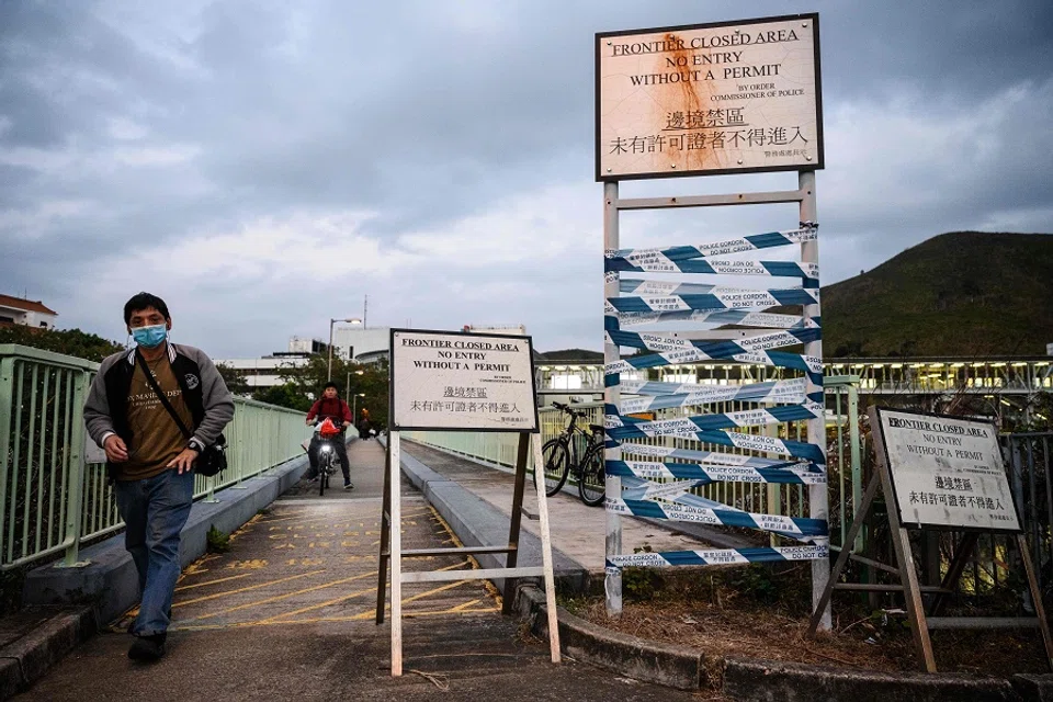 This photo taken on 6 February 2020 shows people crossing a bridge that can be used only by villagers with a special permit, within a Frontier Closed Area from Lo Wu MTR station in Hong Kong and buildings (back) behind the Hong Kong border fence in Shenzhen, China. The border crossing is currently closed as part of government measures to control the spread of the Covid-19. (Anthony Wallace/AFP)