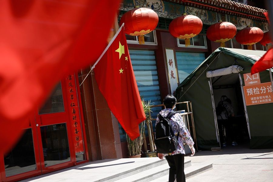 A woman walks outside a traditional Chinese medicine hospital decorated with a Chinese flag following the coronavirus outbreak, in Beijing, China on 19 May 2020. (Tingshu Wang/Reuters)