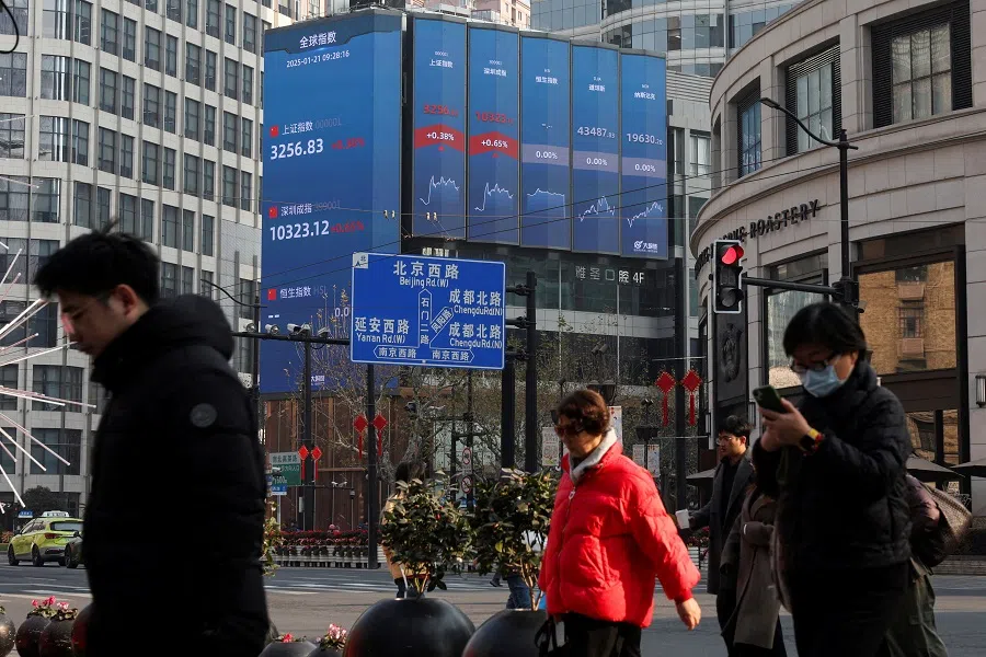 Pedestrians wait for a street signal on a sidewalk as an electronic billboard shows the Shanghai and Shenzhen stock indexes in Shanghai, China, on 21 January 2025. (Go Nakamura/Reuters)